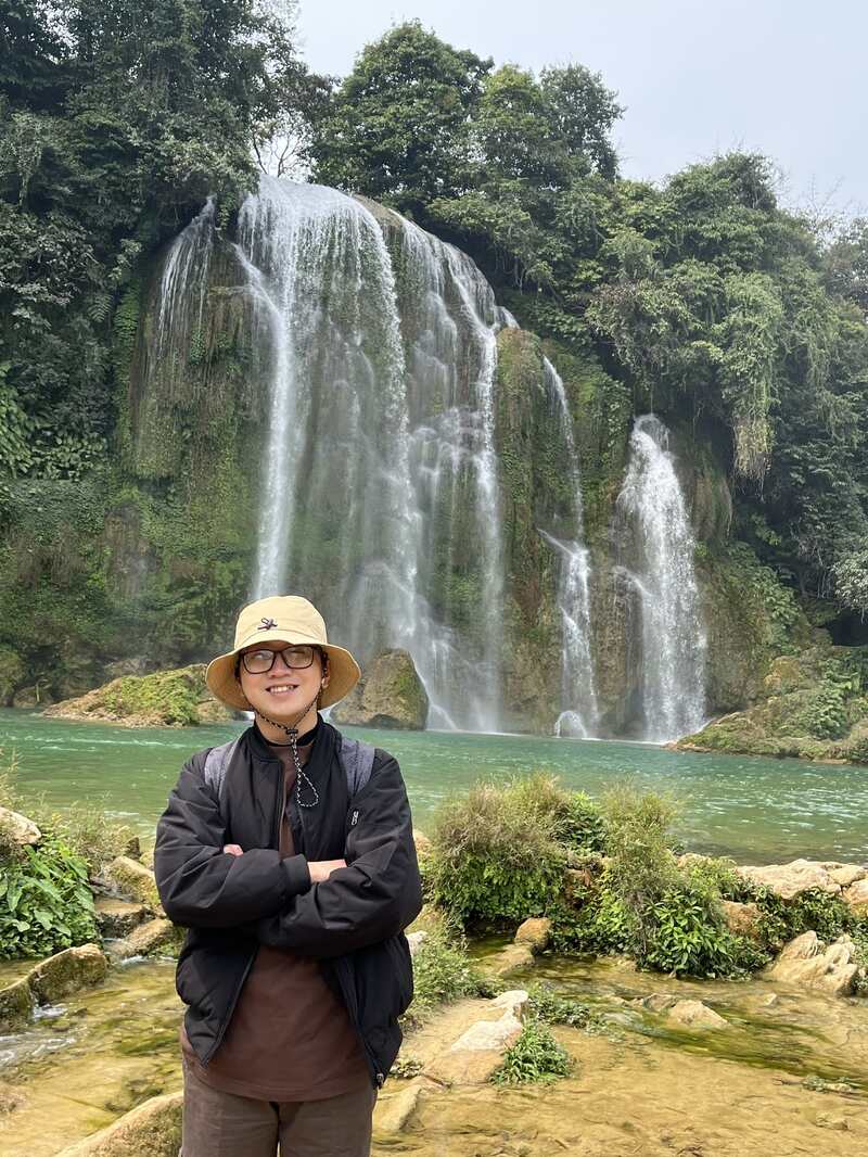 Photo of Oliver Phung standing in front of the waterfall at Ban Gioc.